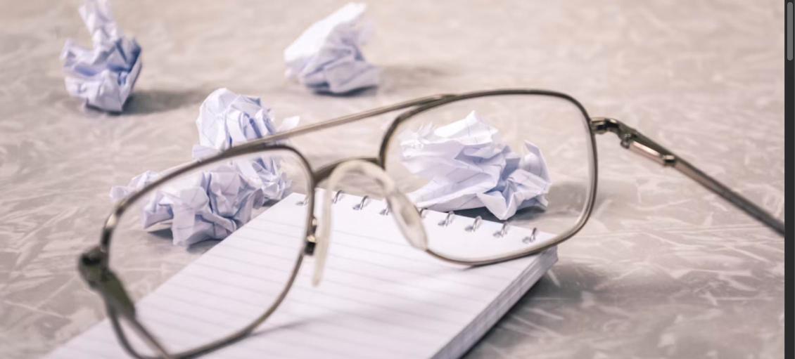 Crumpled paper balls and eyeglasses on a notebook, representing cover letter mistakes
