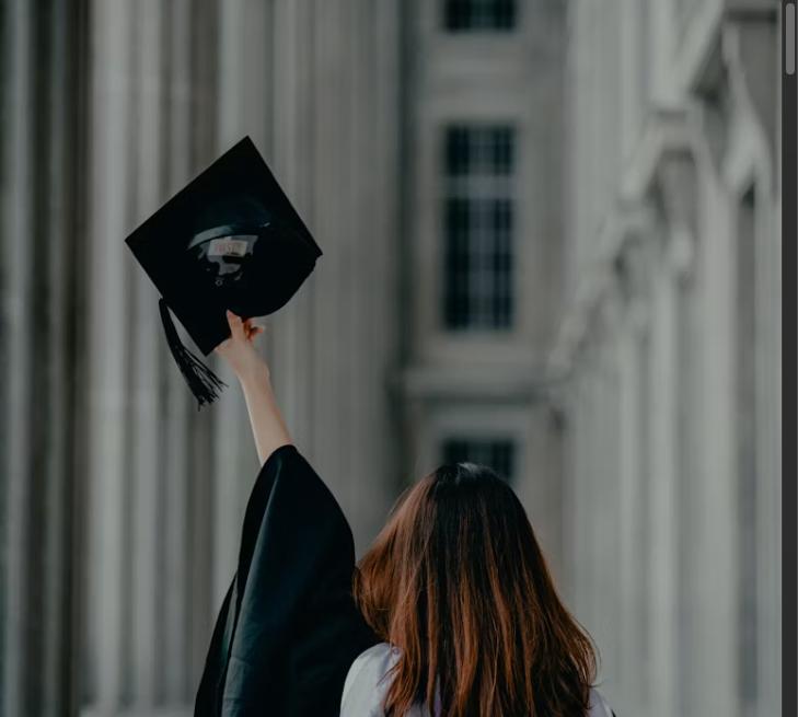 College graduate raising a graduation cap outside a university building