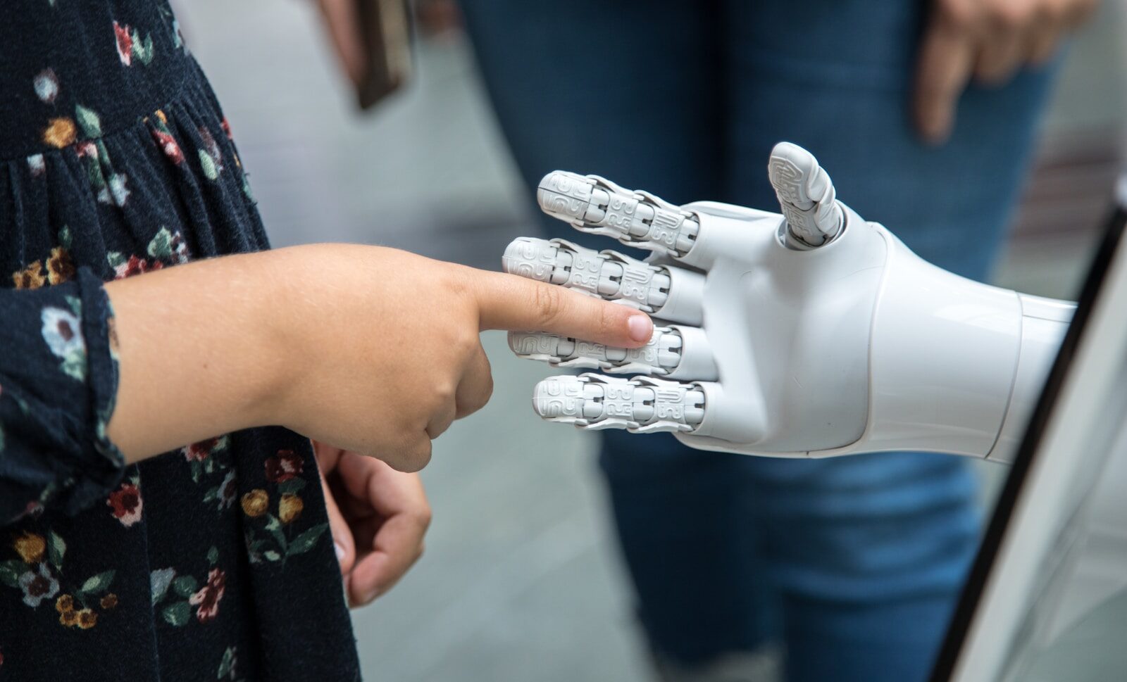 A human finger touching a robotic hand, representing whether AI will replace human recruiters