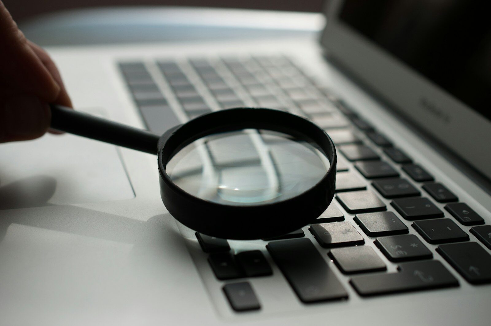 Magnifying glass over a laptop keyboard, representing recruiters searching for candidate profiles