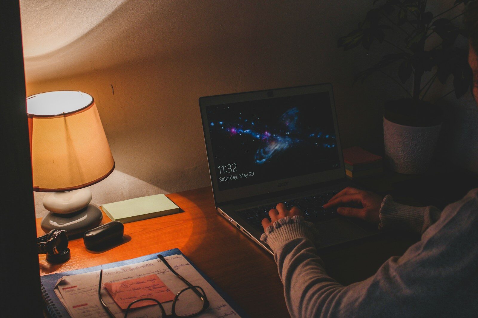 Person job searching on a laptop late at night by lamplight, balancing it with a full-time job