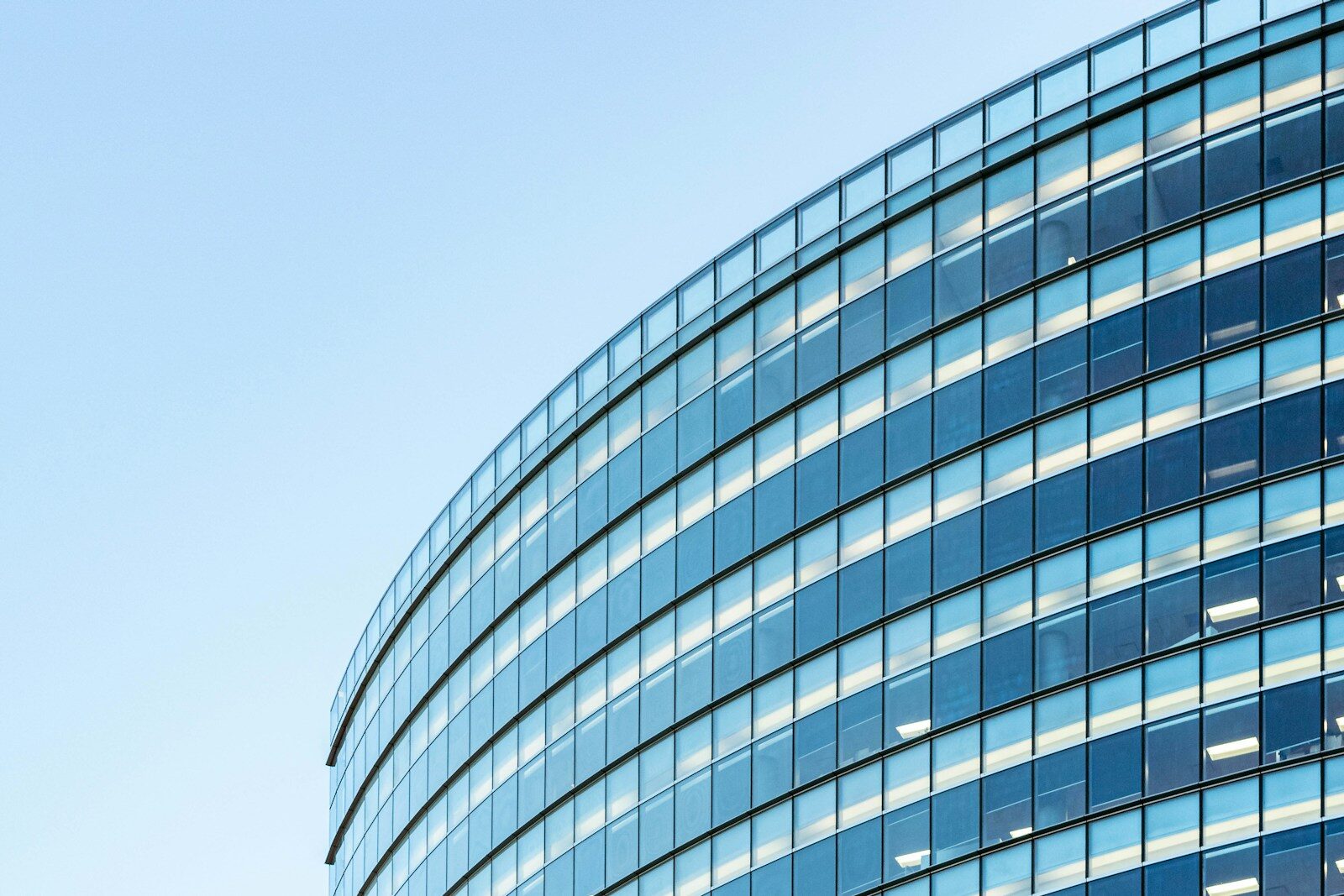 white and blue glass walled buildinModern curved glass office building exterior, representing a company workplaceg