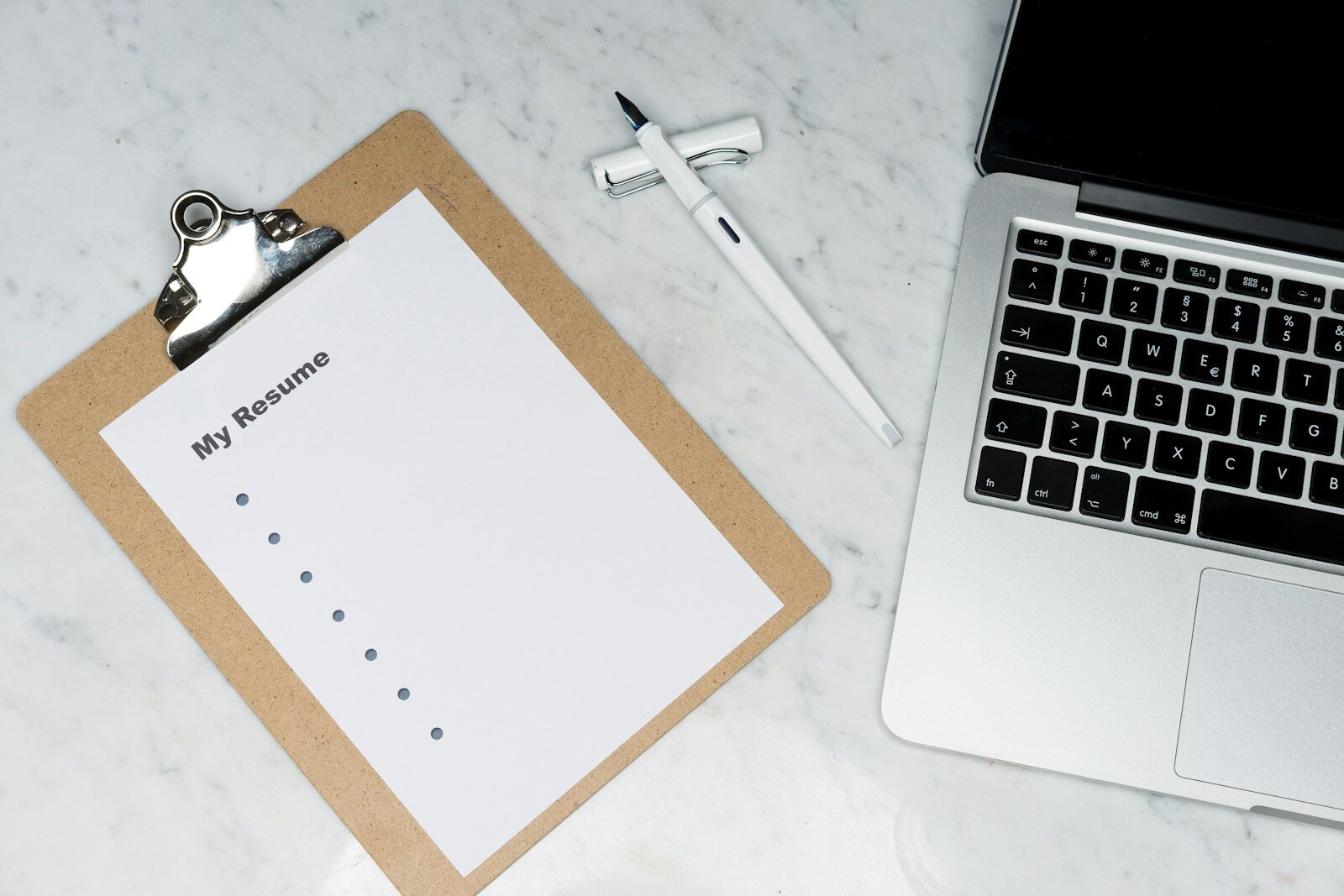 Clipboard with a resume beside a laptop, illustrating how far back should your resume go
