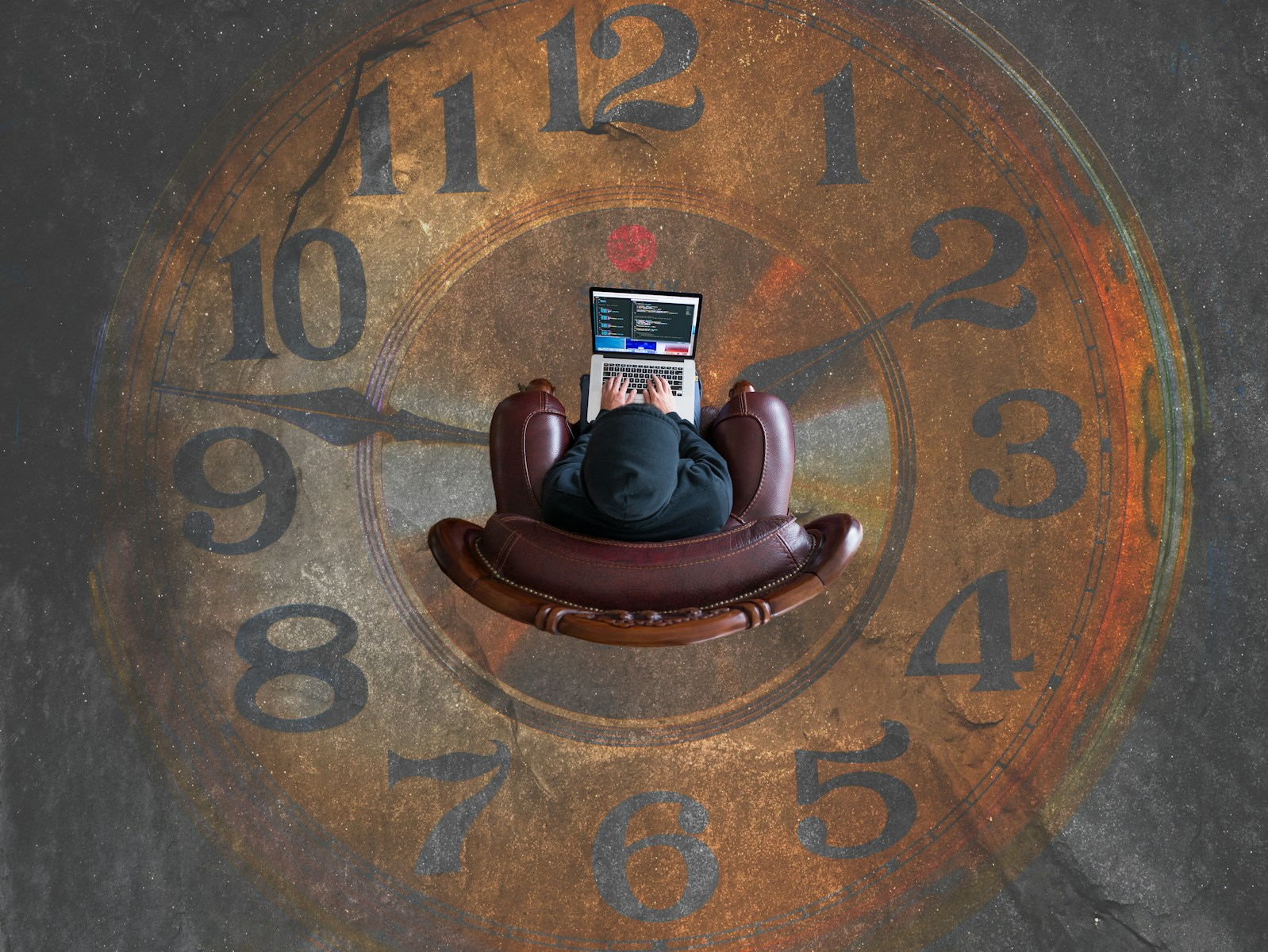Time vampires: an office worker sitting in a chair at the center of a giant clock face while working on a laptop, illustrating time slipping away