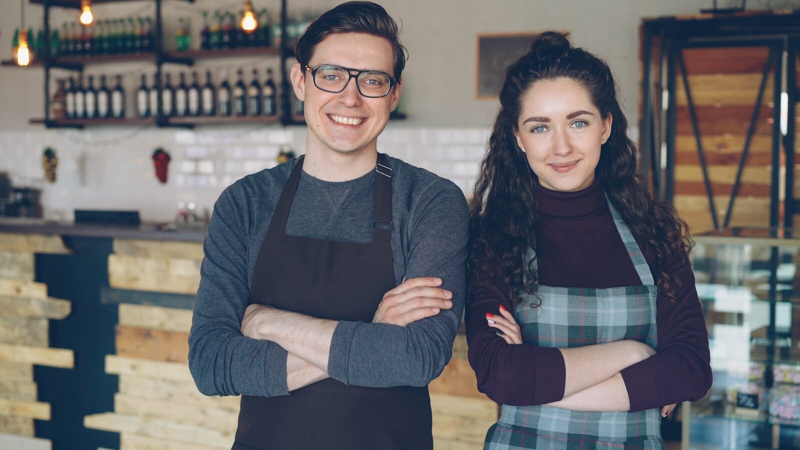 Small business jobs: two small business owners, a man and woman in aprons, standing together in their café storefront