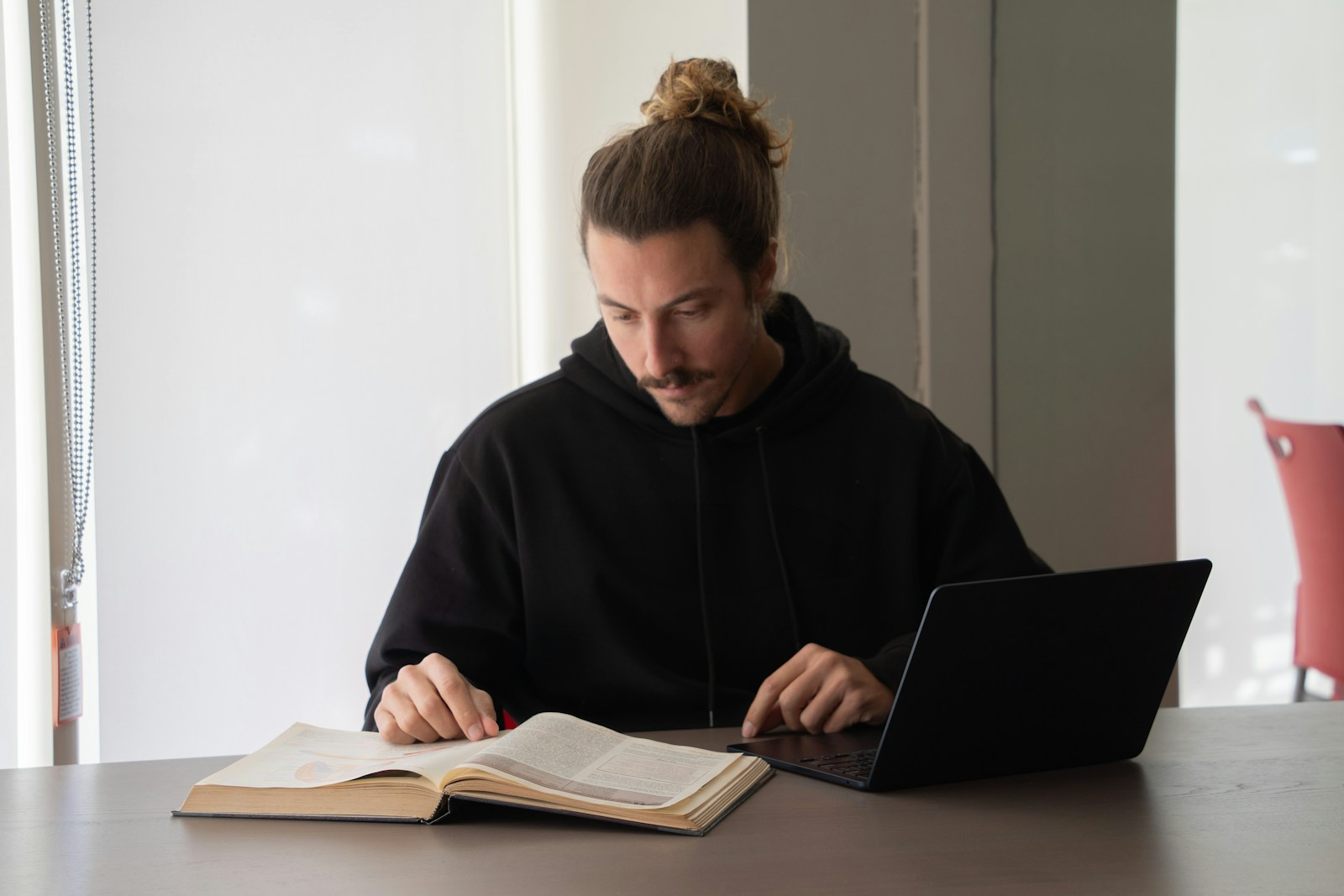 A person reading a book while researching on a laptop, representing the certification research stage of preparing to teach English abroad