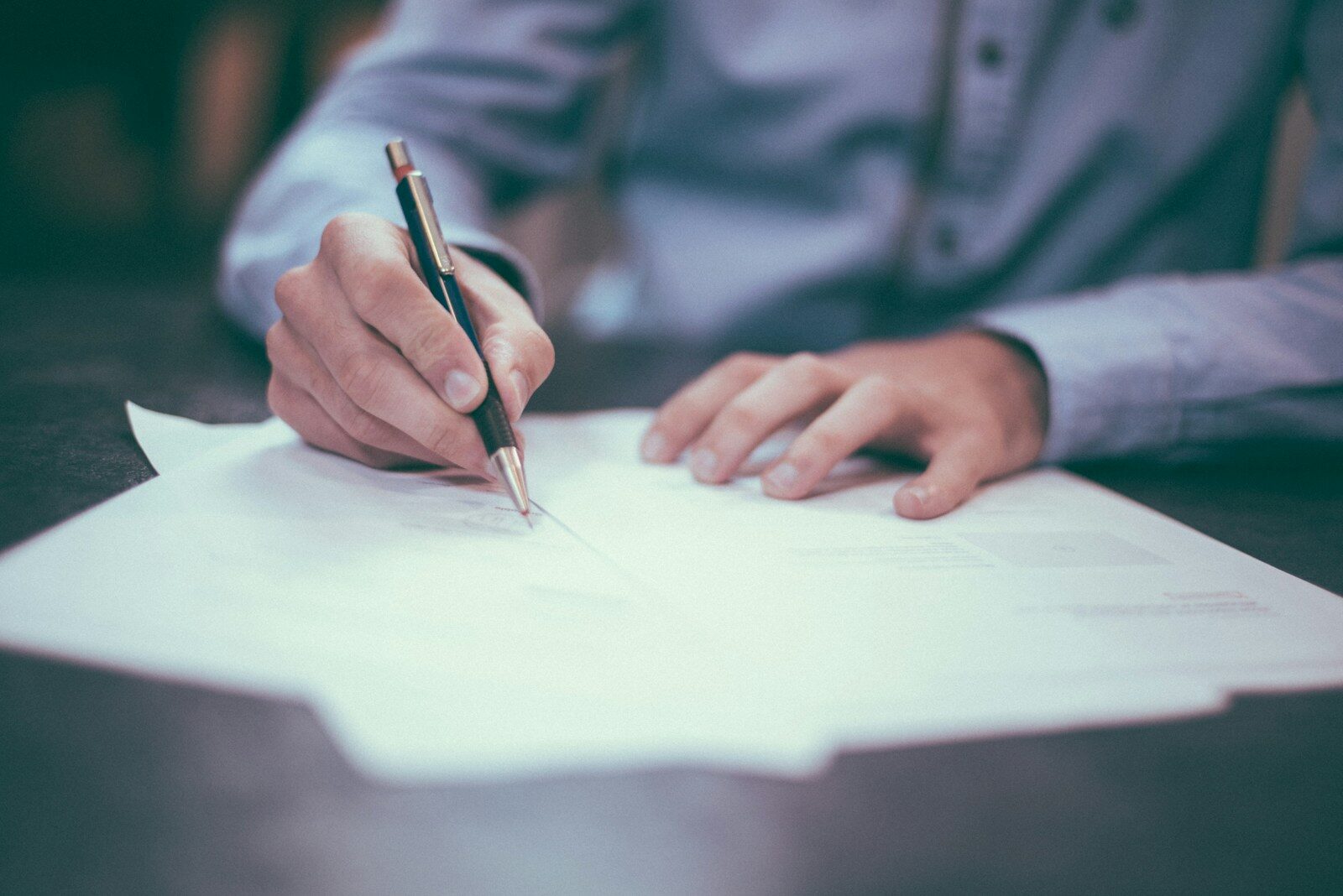 A person signing paperwork, representing the careful review a teaching contract deserves before signing