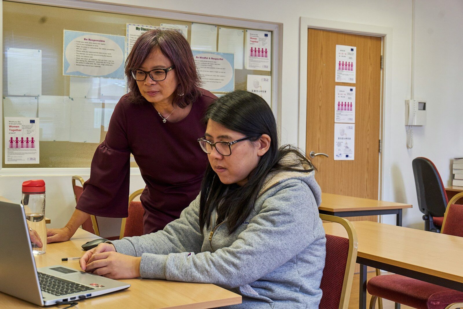 A tutor working one-on-one with a student on a laptop, representing the specific subject focus that matters when starting a tutoring business