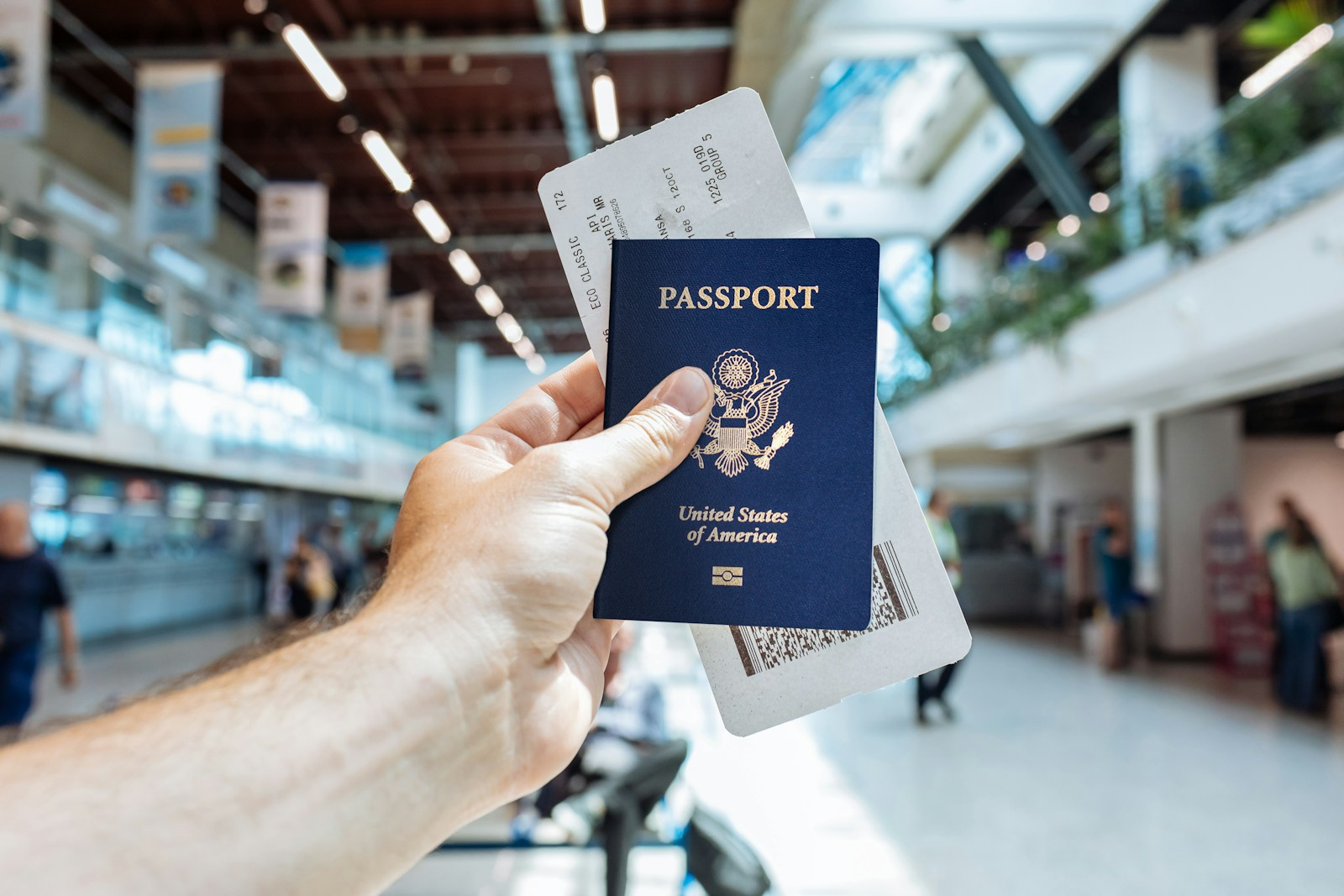 A hand holding a U.S. passport at an airport, representing the visa and travel logistics of moving abroad to teach English